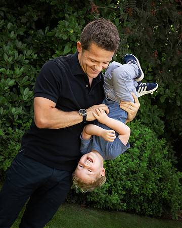 A dad holds his pre-school-aged son upside-down while he gigles