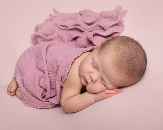 Newborn baby curled up asleep on her front
