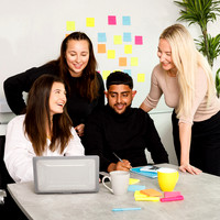 Groups of people smiling, drinking coffee and looking at the laptop on the desk.