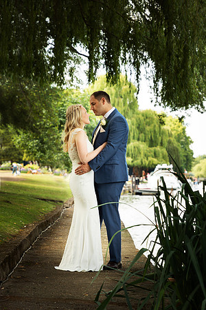 A bride and groom hold each other under a weeping willow alnogside the Thames at Windsor's Oakley Court
