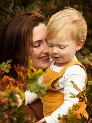 a mother cuddles her son, photographed outdoors in autumnal colours with autumnal oak leaves in the foreground