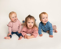 Three siblings (baby twins and toddler girl) smile sitting together