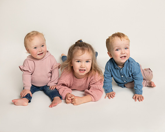 Three siblings (baby twins and toddler girl) smile sitting together
