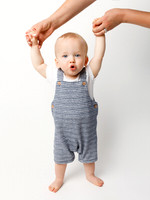 A baby aged around one year stands whilst holding his parent's hands (just in shot) and makes a cue 'ooh' expression