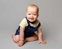 A baby boy photographed sitting up and looking at the camera with a cheeky smile