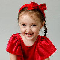 A three-year-old girl gives a big smile to the camera, dressed in red with a red bow on her hair