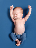 A baby dressed only in little blue trousers, stretches in his sleep, laying on a blue blanket
