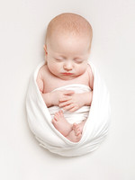A baby wrapped in a white blanket, laying on a white backdrop, sleeping peacefully