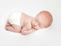 A baby curled up on his front wearing a pair of knitted white bloomers