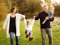 Parents holding their daughter's hand walk along and swing her, the father is also holding his toddler daughter
