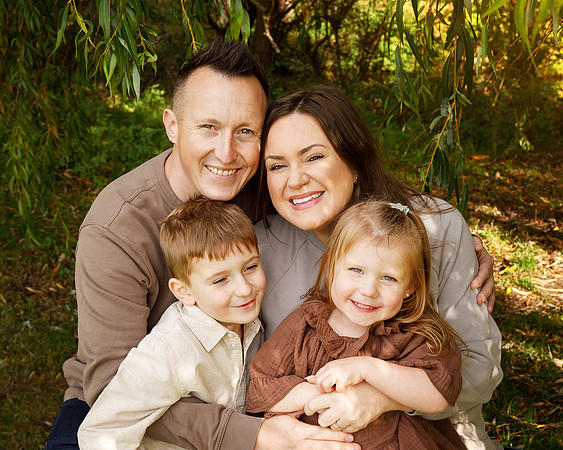 A family of four cuddle close together, photographed up close under a willow tree