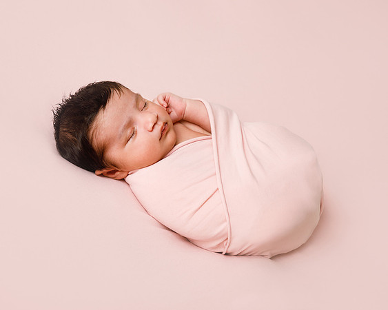 Newborn baby girl wrapped in a pink blanket laying on a matching backdrop