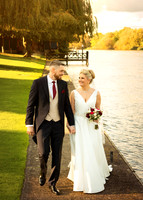 A bride and groom stroll along the riverside at Oakley Court