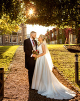 A bride and groom smiles at each other as the autumn sun shines through the trees in the grounds of Oakley Court