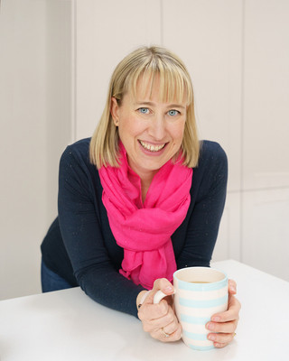 Abi Moore, brand photographer, photographed in a kitchen smiling at the camera holding a cup of tea.