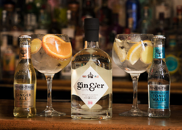 Gin bottle alongside two gin glasses with garnishes and bottles of tonic