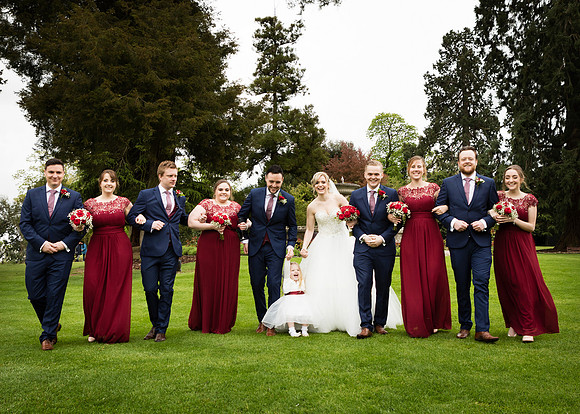 A bridal party walk arm-in-arm through the grounds of Oakley Court
