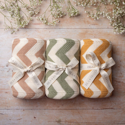 Three chevron blankets from Isla & Fraser phtoographed in a row on wood with gypsophilia