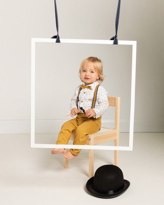 Toddler boy in smart outfit sits on a chair surrounded by photo booth props
