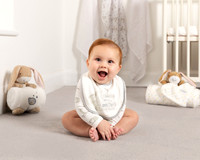 Sitting baby smiles at the camera surrounded 'Guess How Much I Love You' baby products