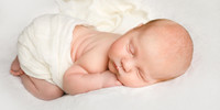 Sleeping baby photographed during a newborn shoot wrapped in a cream muslin