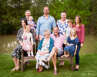 Three generations of a family photographed together gathered on and around a bench by a lake