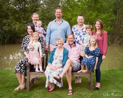 Three generations of a family photographed together gathered on and around a bench by a lake