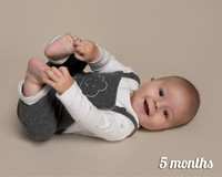 Five month old baby boy lays on his back playing with his toes and smiling at the camera