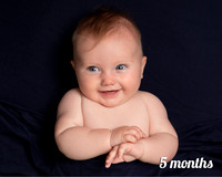 Five month old baby lays on navy blanket and smiles widely