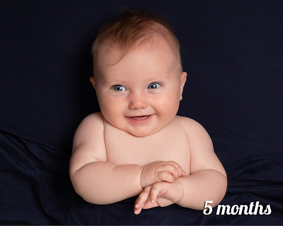 Five month old baby lays on navy blanket and smiles widely