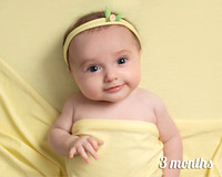 Three month old baby girl laid on yellow smiles straight at the camera