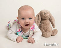 Four month old girl smiles laying on her front next her rabbit teddy
