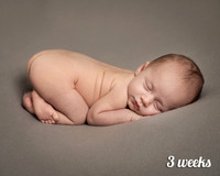 Three-week-old baby lays on his front curled up asleep