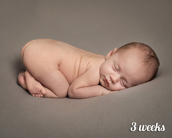Three-week-old baby lays on his front curled up asleep