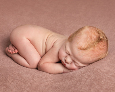 One week old baby lays curled up asleep on her front