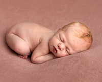 Newborn baby, a few days old, photographed asleep and curled up on her front