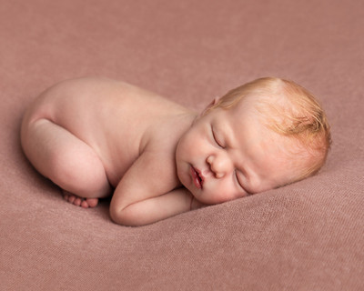 Newborn baby, a few days old, photographed asleep and curled up on her front