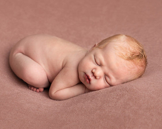 Newborn baby, a few days old, photographed asleep and curled up on her front
