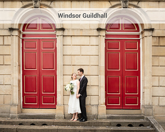 A wedding couple look at each other whilst holding hands framed by the red doors of Windsor's Guildhall