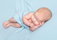 Newborn baby boy laying on his side on a blue backdrop with a blue backdrop draped over him