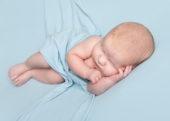Newborn baby boy laying on his side on a blue backdrop with a blue backdrop draped over him