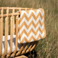 A chevron blanket draped over a wooden cot in a long grass meadow