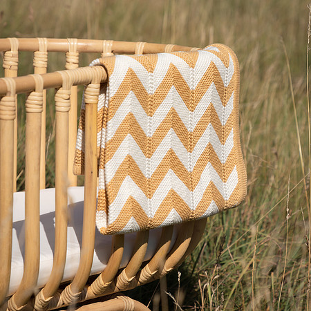 A chevron blanket draped over a wooden cot in a long grass meadow