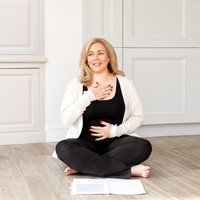 Lady sitting cross legged on the floor addressing her yoga class