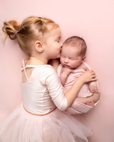 Little girl in a tutu hugs her newborn baby sister during a photoshoot
