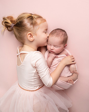 Little girl in a tutu hugs her newborn baby sister during a photoshoot
