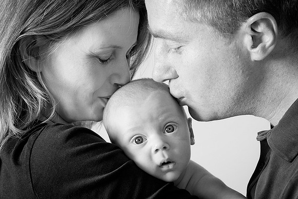 Parents kiss 12-week-old baby during photoshoot - baby looks surprised