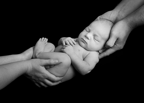 Newborn baby boy held in his parents' hands, photographed in black & white