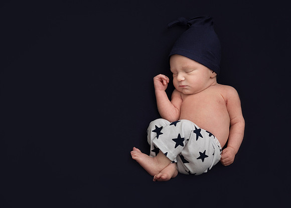 Newborn baby boy asleep on navy blanket wearing star trousers and navy hat during newborn photo shoot