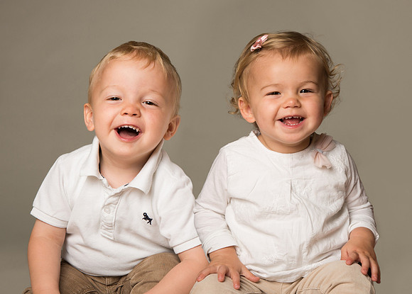 Twin boy and girl giggle whilst being photographed in a studio setting